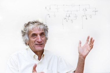 <p>John Martinis posa en el ICMAT delante de un esquema de circuitos dibujado por él mismo. / Álvaro Muñoz Guzmán (SINC)</p>